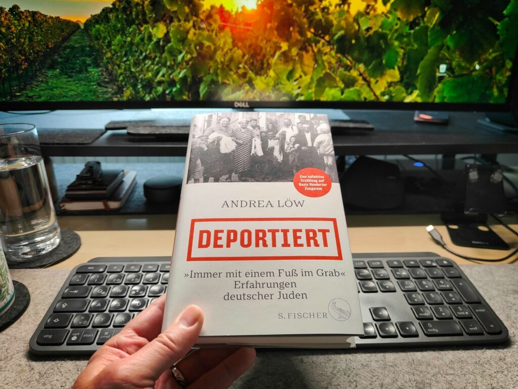 "Deportiert" - das Buch von Andrea Löw in der Hand gehalten vor einer Tastatur und einem Display